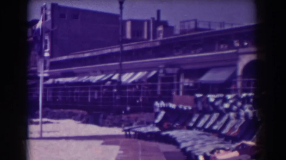 1938 Atlantic City boardwalk view with empty lounge chairs, striped awnings, railings, and arched building fronts.