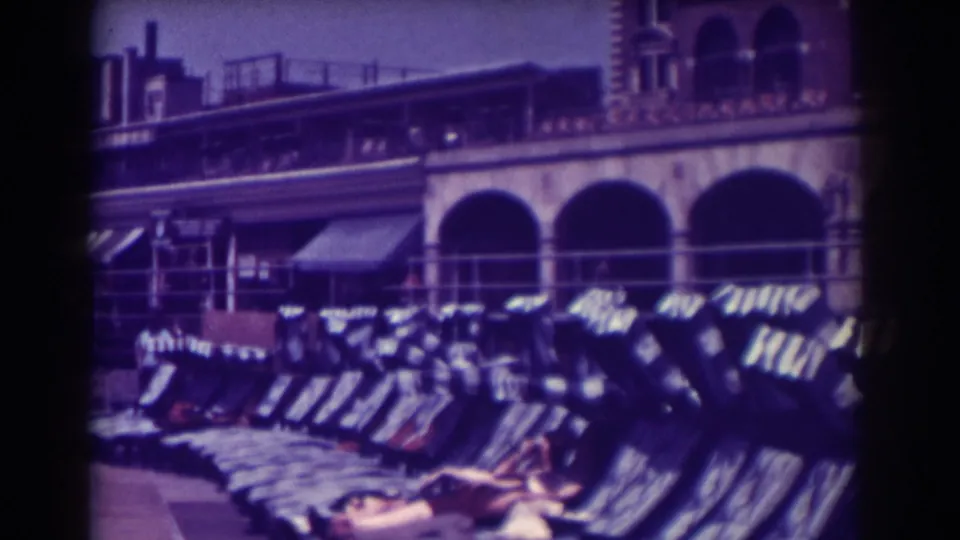 A woman in swimwear reclines on a lounge chair at Atlantic City, with rows of chairs and arched boardwalk architecture behind her.