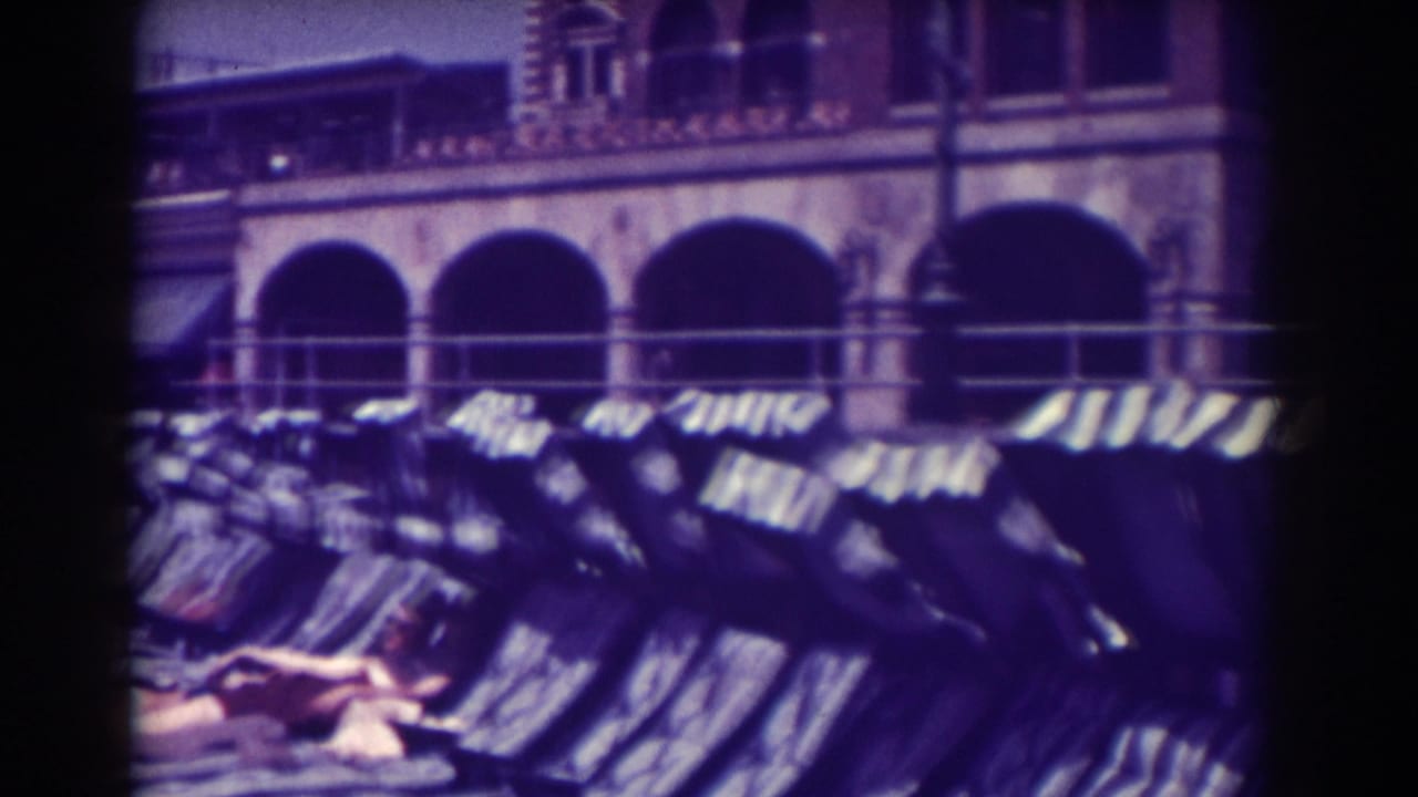 Rows of empty lounge chairs beneath striped awnings in front of an arched building.