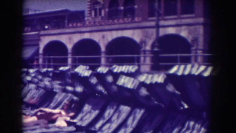 1938 Atlantic City boardwalk view with empty lounge chairs, striped awnings, railings, and an arched building facade behind them.