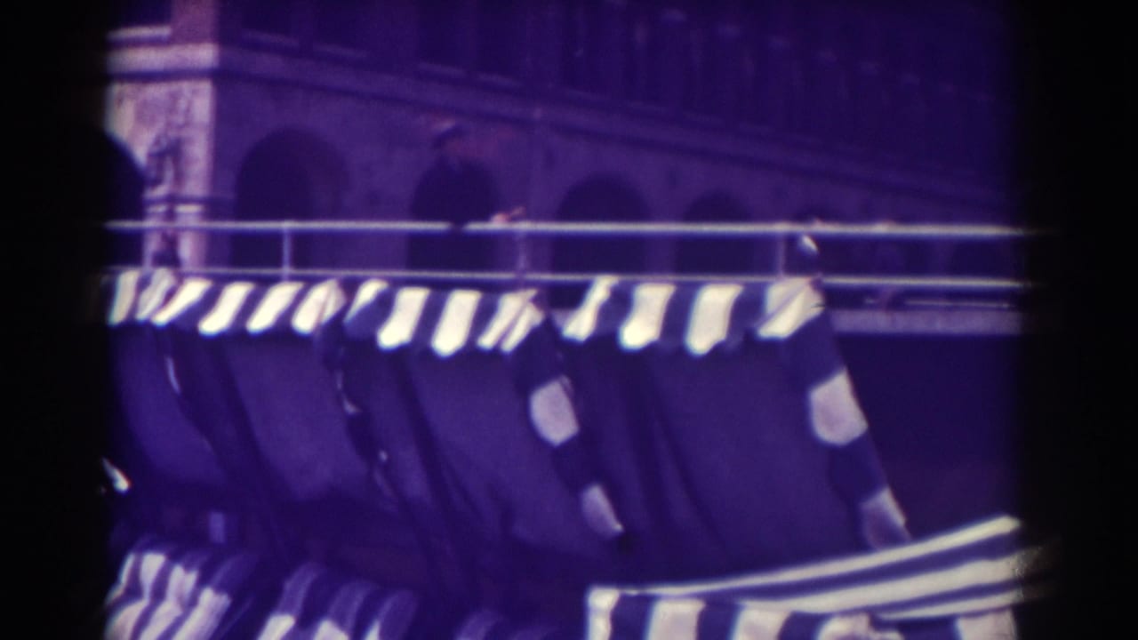 Striped awnings and beach chairs along a boardwalk beneath an arched building facade.