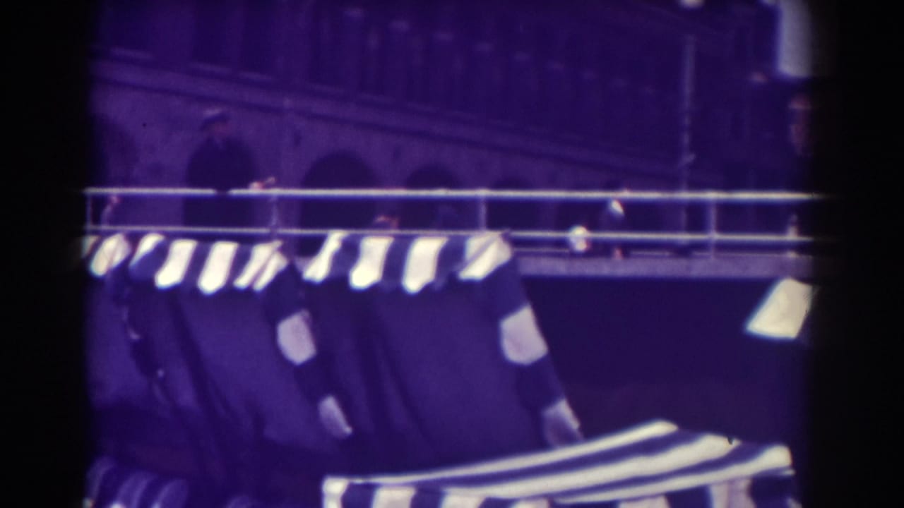 Atlantic City boardwalk seating and striped awnings seen from a handheld 8mm viewpoint, with building arches behind.