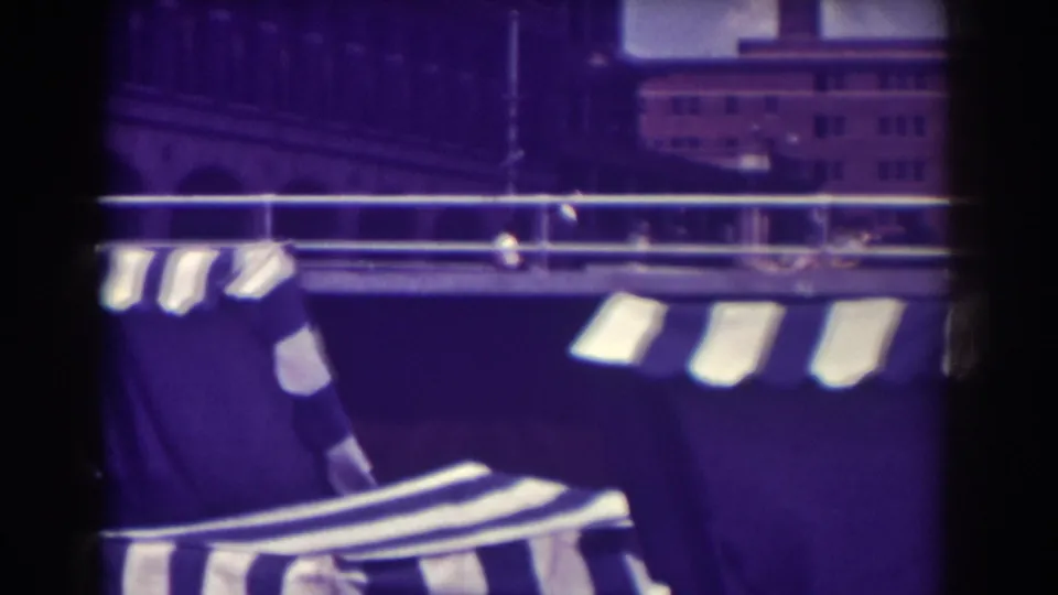 Close view of Atlantic City boardwalk awnings and lounge chairs, with railing and a distant building visible through aged purple film color.