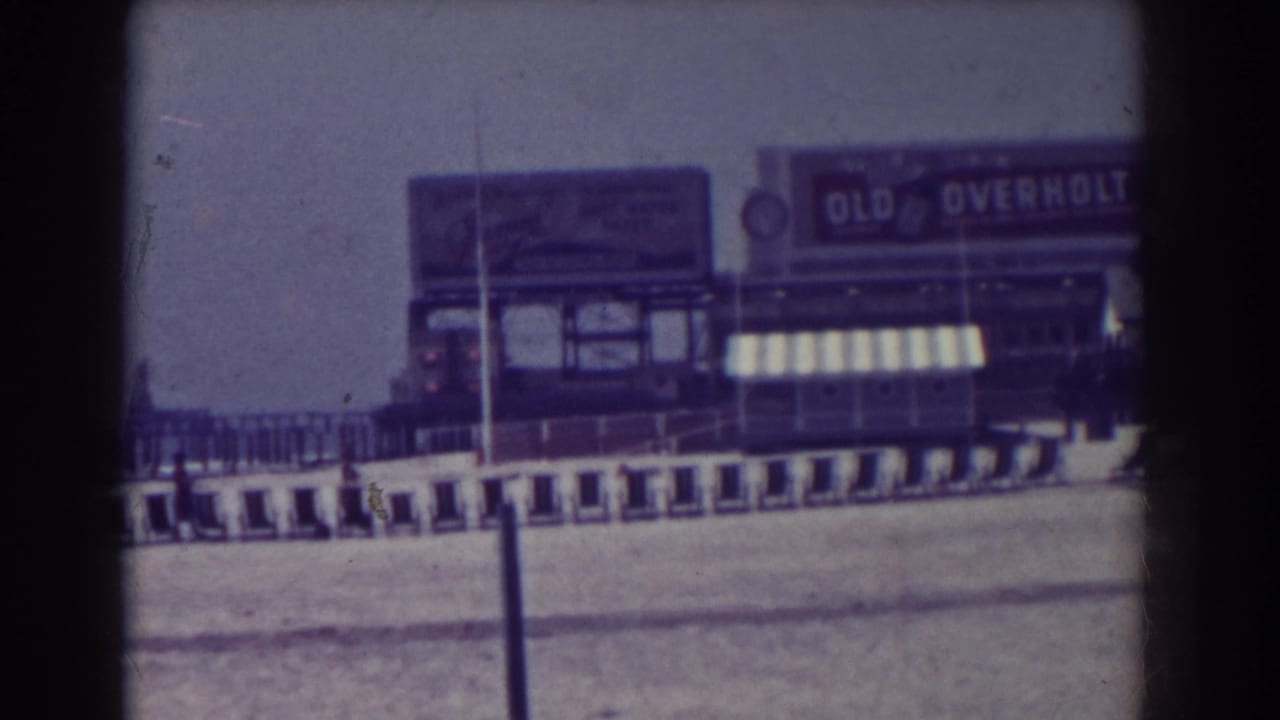 Boardwalk storefronts with an Old Overholt sign and striped awning above railings.