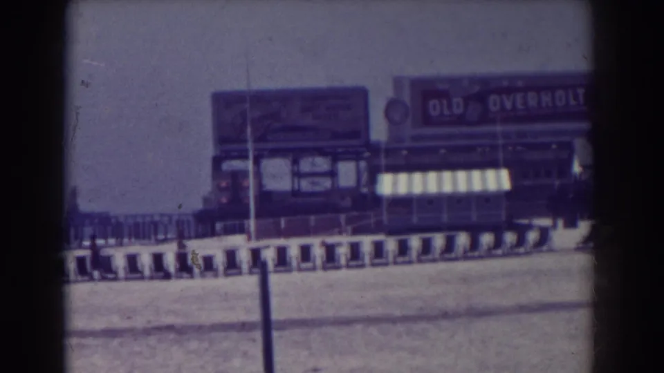 1938 Atlantic City boardwalk view with visible Old Overholt signage, storefront awnings, railings, and soft 8mm film color.