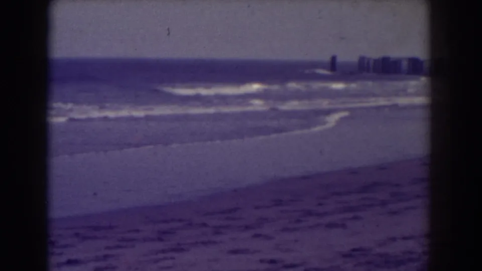 Atlantic City ocean view on 8mm film, showing low waves, sand, and distant shoreline buildings under hazy light.