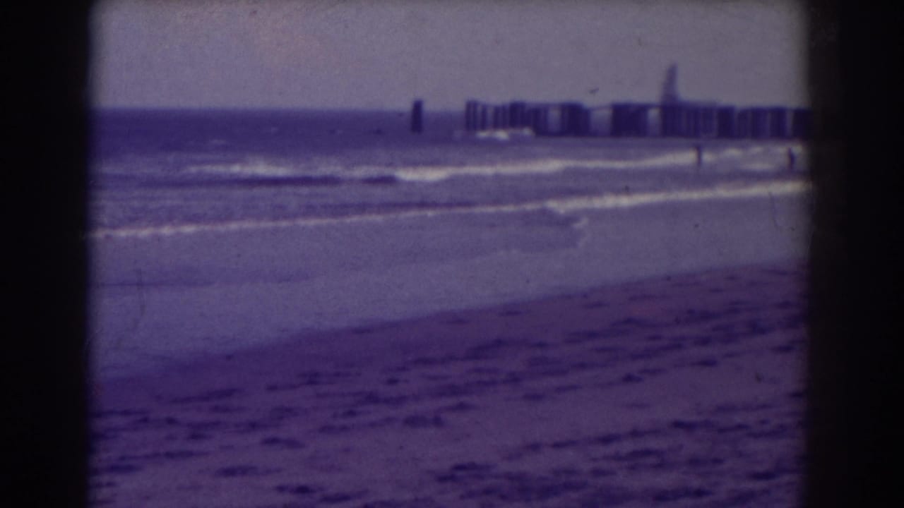 Waves roll onto a sandy beach with a pier visible in the distance.