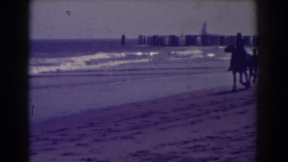 1938 Atlantic City beach frame showing two small walking figures near the waterline, with surf and a distant pier behind them.