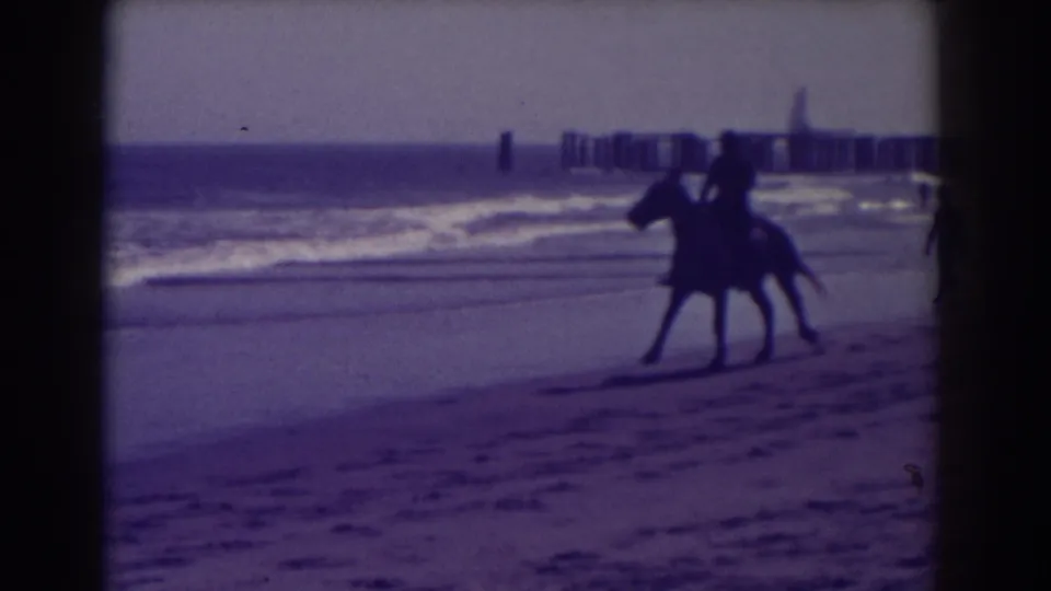 1938 Atlantic City beach scene with a horse and rider near the waterline and a distant pier or jetty in the background.