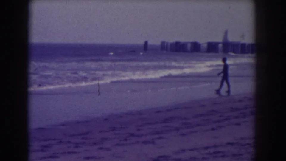 A solitary beachgoer walks along the 1938 Atlantic City shoreline, with surf and a distant pier structure beyond.