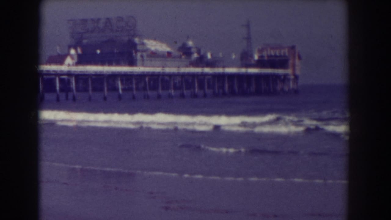 Pier over the surf with rooftop signs and dark film borders.