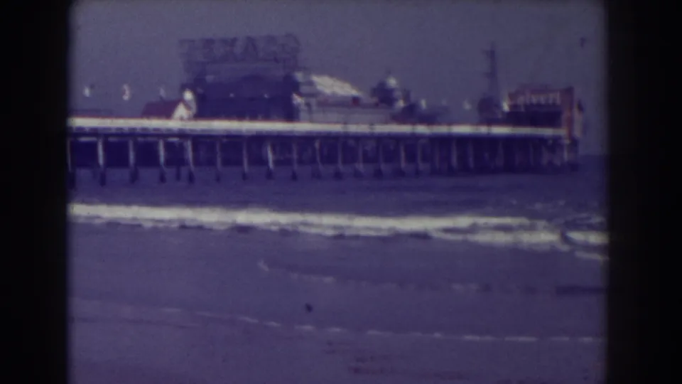 Atlantic City 8mm frame showing the pier and pilings above low surf, with signs and structures softened by film grain.