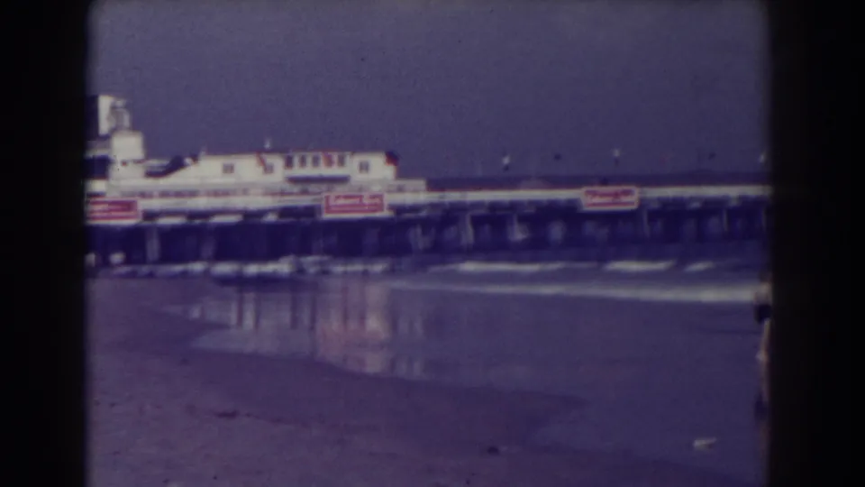 1938 Atlantic City beach view with wet sand, low waves, and a pier or boardwalk building carrying visible signage.