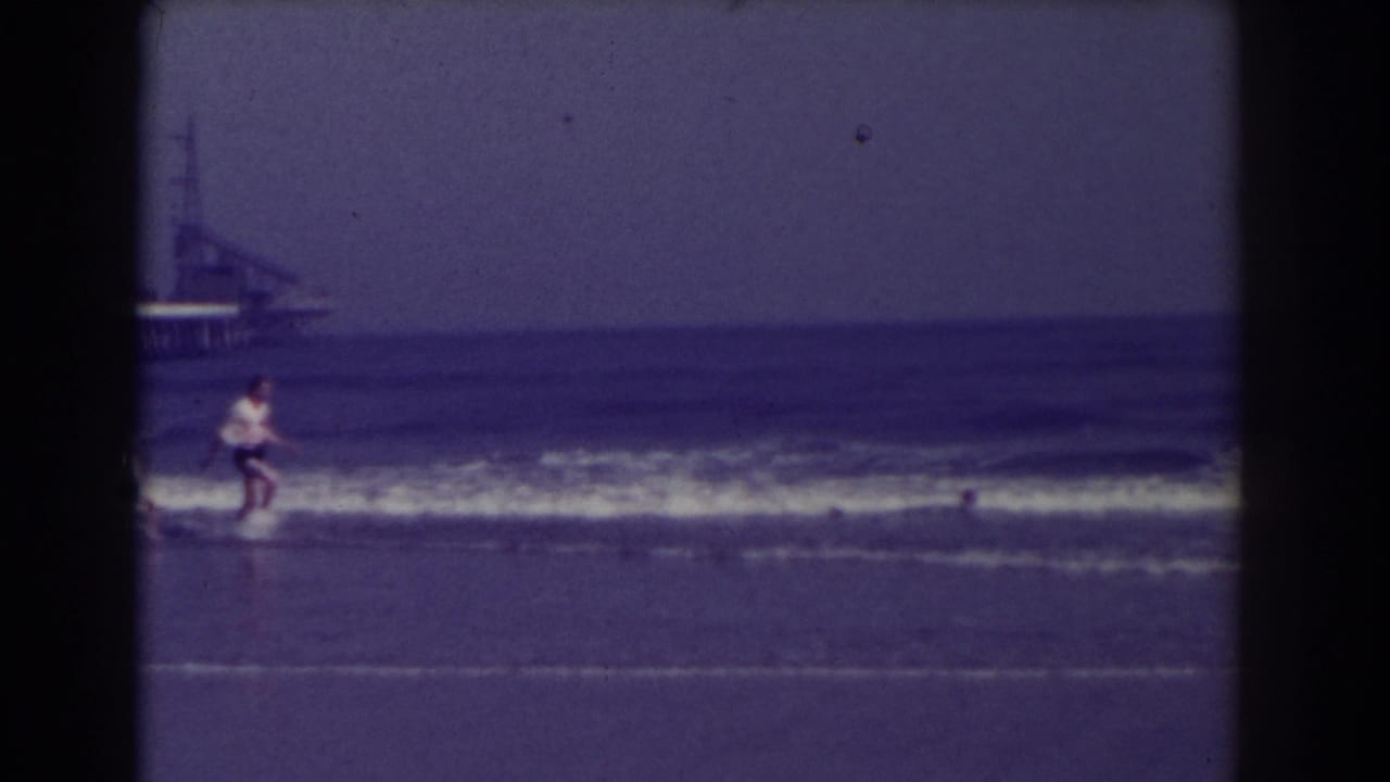 Beachgoer running near the surf with a pier in the distance.