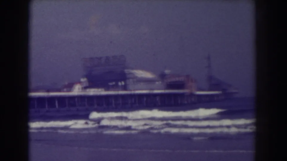 1938 Atlantic City 8mm frame showing small ocean waves, a long pier on pilings, hazy sky, and buildings at the pier end.