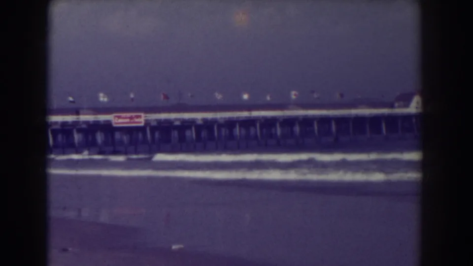 1938 Atlantic City view of waves reaching the shore below a long flagged pier, with the Texaco sign visible near the center.