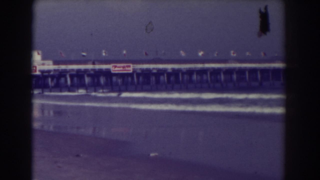 Distant pier over surf with flags and signs above a wet Atlantic City beach.