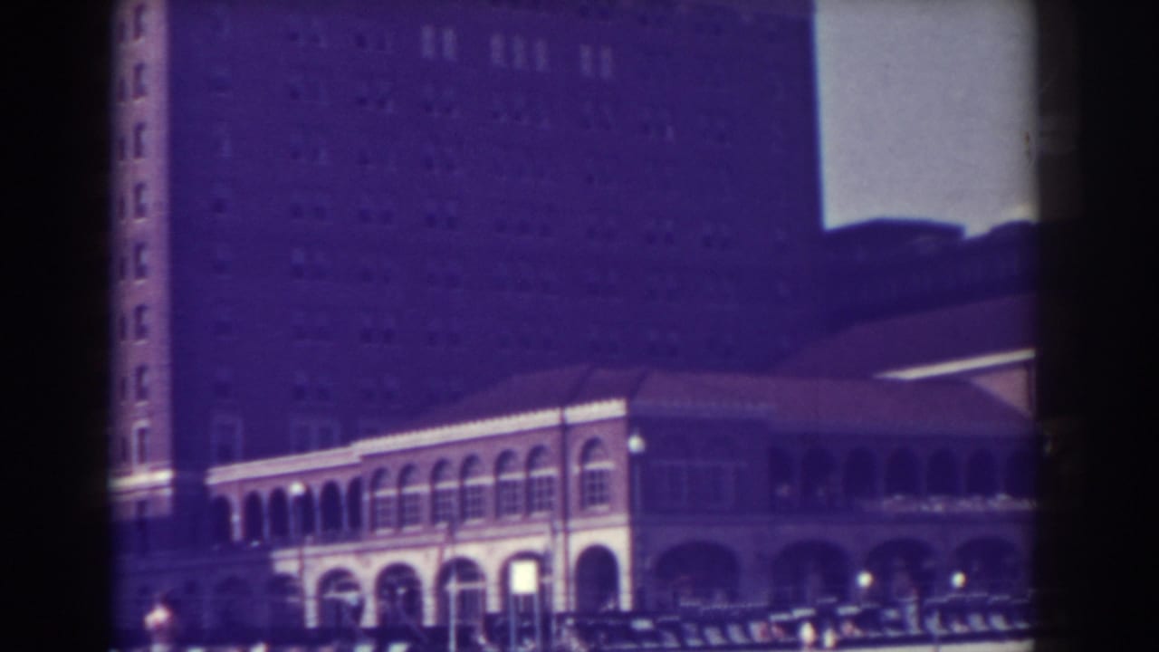 Arched public building facade with tall tower behind and cars along the street.