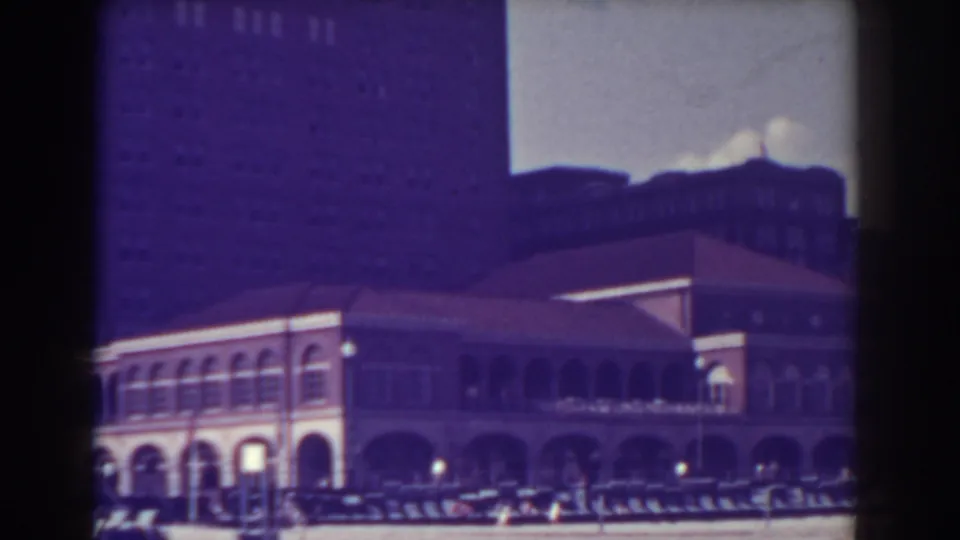 Home-movie frame of the Brown Public City Library in Atlantic City, with its arched facade, street lamps, cars, and people visible at a distance.
