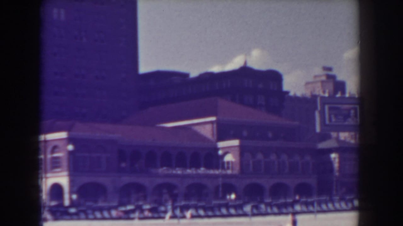 Arched boardwalk building along a beach with distant people and soft rooftop silhouettes.
