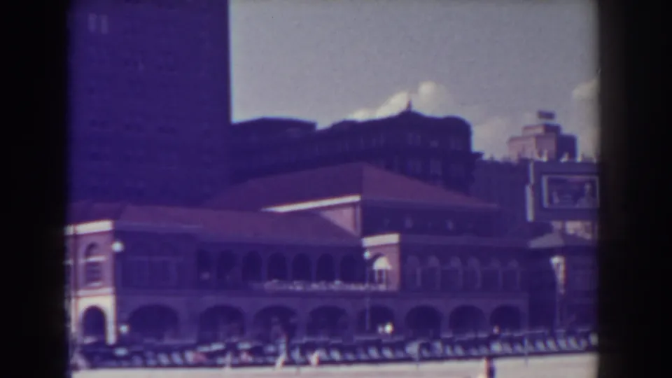 1938 Atlantic City home-movie frame showing an ornate arched boardwalk building beside the beach, with distant pedestrians and soft film color shift.