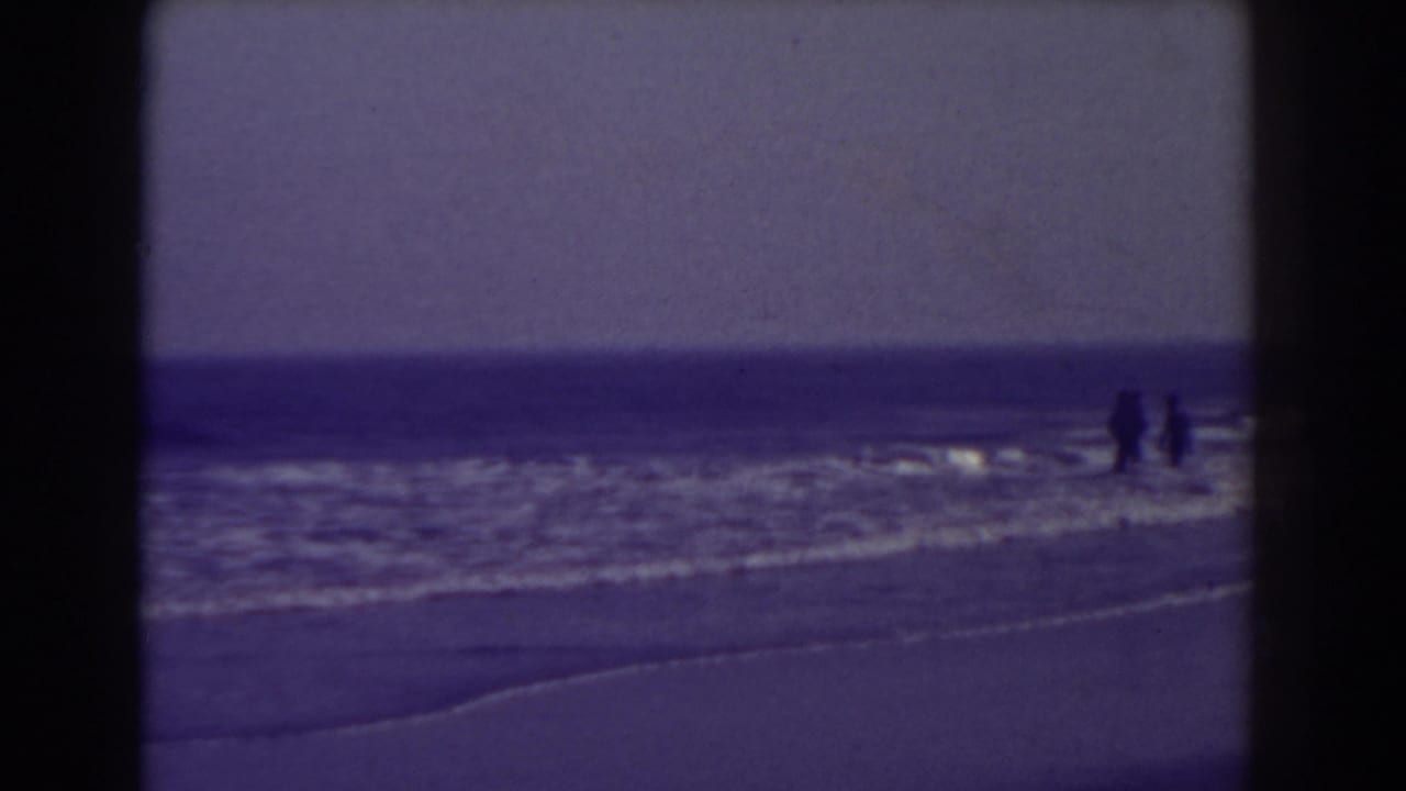 Distant people walking in shallow surf along a beach with ocean horizon.
