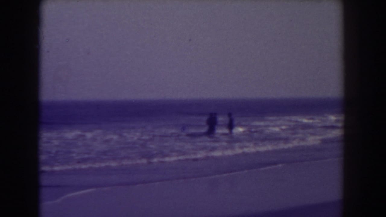 Distant beachgoers appear in shallow Atlantic City surf, framed by blue-toned 8mm film borders.