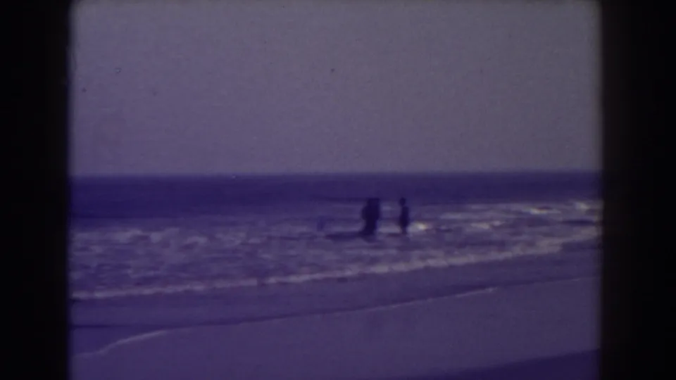 Distant beachgoers appear in shallow Atlantic City surf, framed by blue-toned 8mm film borders.