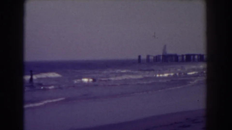 Atlantic City shoreline in 1938 with a lone distant beachgoer near the waves and a pier extending into the ocean.