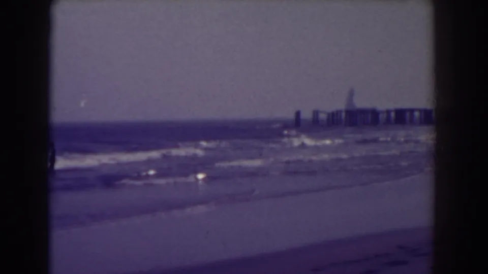 1938 home-movie view of Atlantic City surf and beach, with the pier softened by grain and distance.