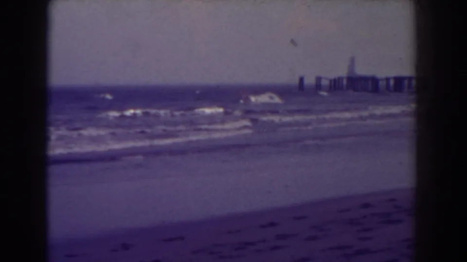 Atlantic City beach and surf in a soft 1938 8mm frame, with the pier at right and dark film borders visible.
