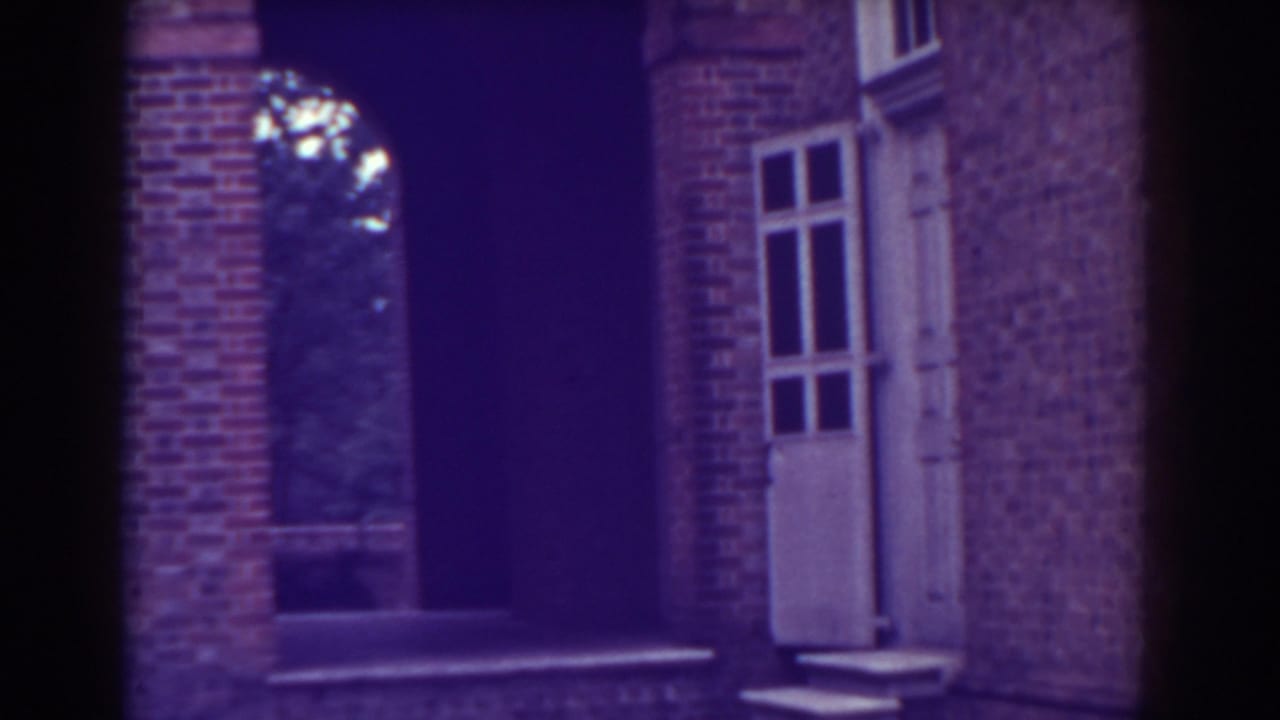 Red brick building entrance with arched opening, columns, steps, and white-framed window.