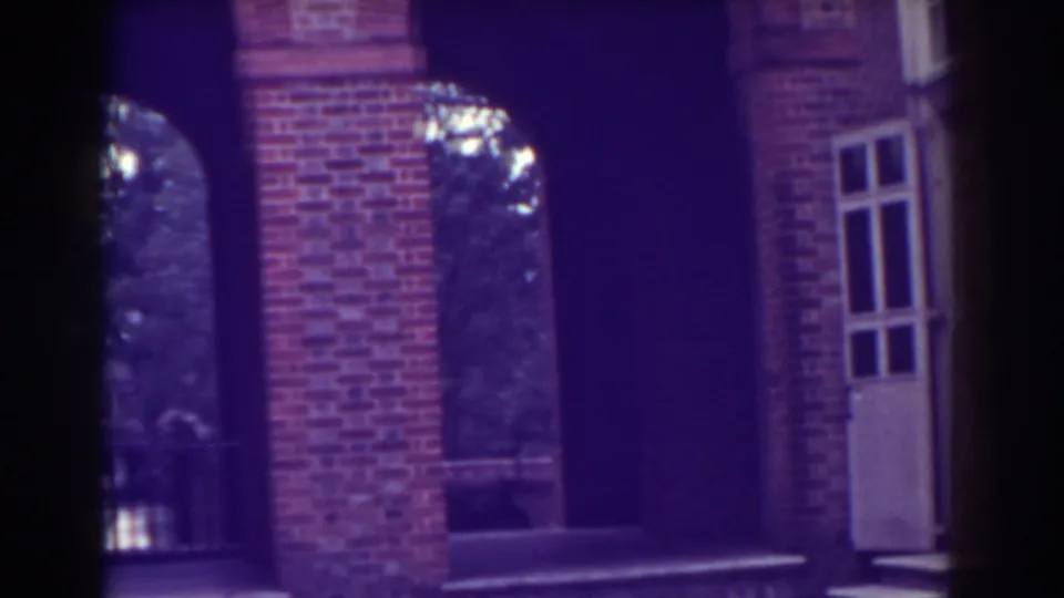 Close 8mm view of the red brick facade, showing an arch, column, white-framed window, dark doorway, and entrance steps.