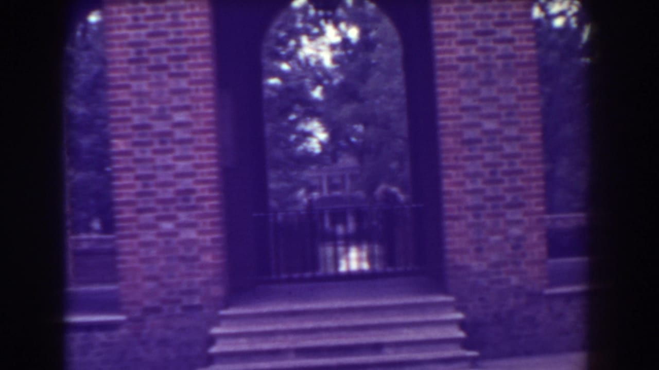 Brick building facade with arched openings, steps, railings, and trees beyond.