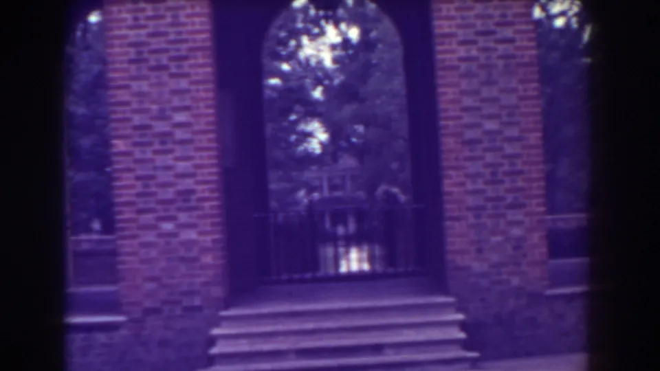 1938 Atlantic City home-movie frame showing a brick facade with tall arches, steps, railings, and trees visible through the openings.