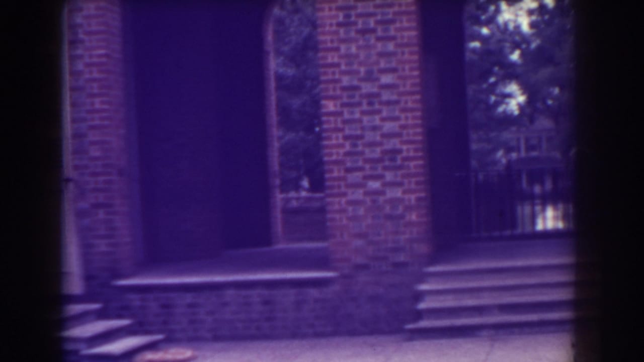 Brick wall with arched doorway, steps, shuttered windows, and trees behind openings.