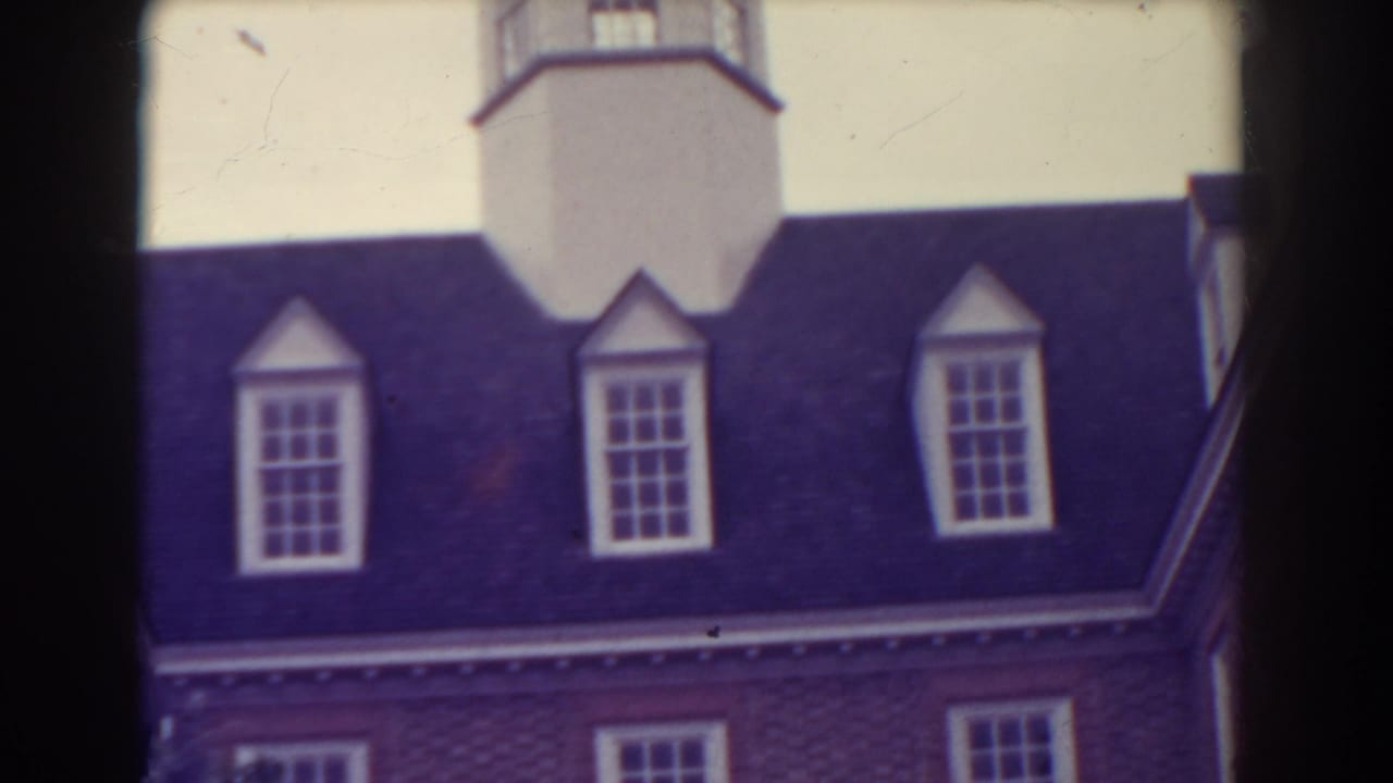 White tower above a dark roof with dormer windows and red brick wall below.