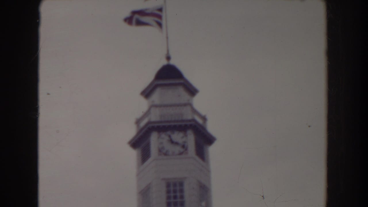 Clock tower with a flag near the top of the frame and dark film border at the side.