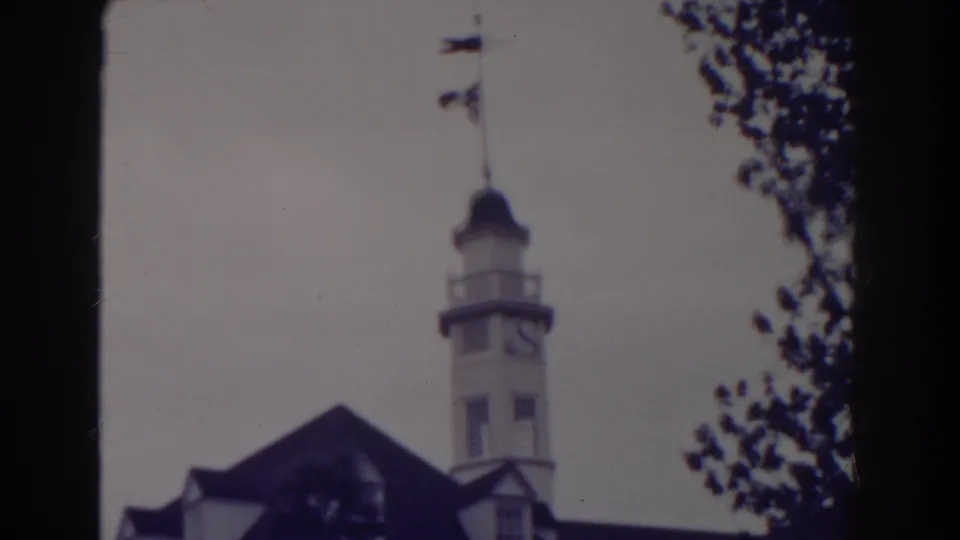 1938 Atlantic City frame centered on a white clock tower rising above a brick building roof, with leafy branches along the edge.
