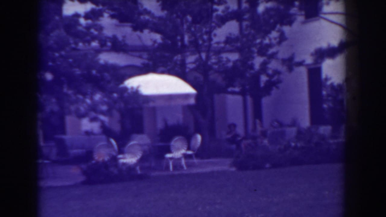 Atlantic City backyard patio in 1938 with white umbrella, outdoor chairs, house facade, trees, and people seated in the background.