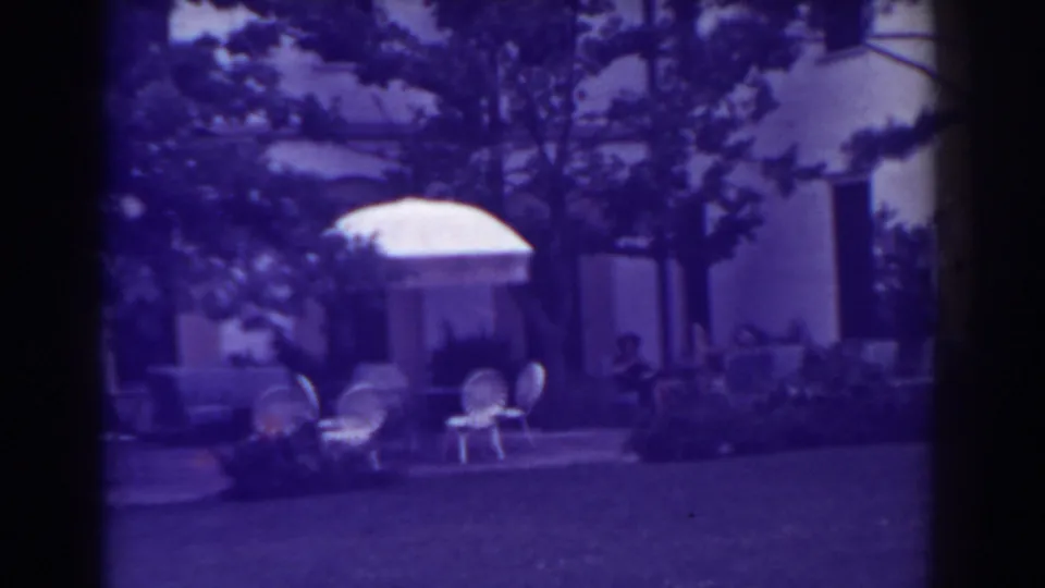 Atlantic City backyard patio in 1938 with white umbrella, outdoor chairs, house facade, trees, and people seated in the background.