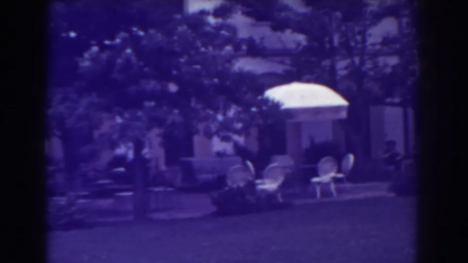 1938 backyard view in Atlantic City showing a lawn, umbrella-shaded patio furniture, trees, shrubs, and the house exterior.