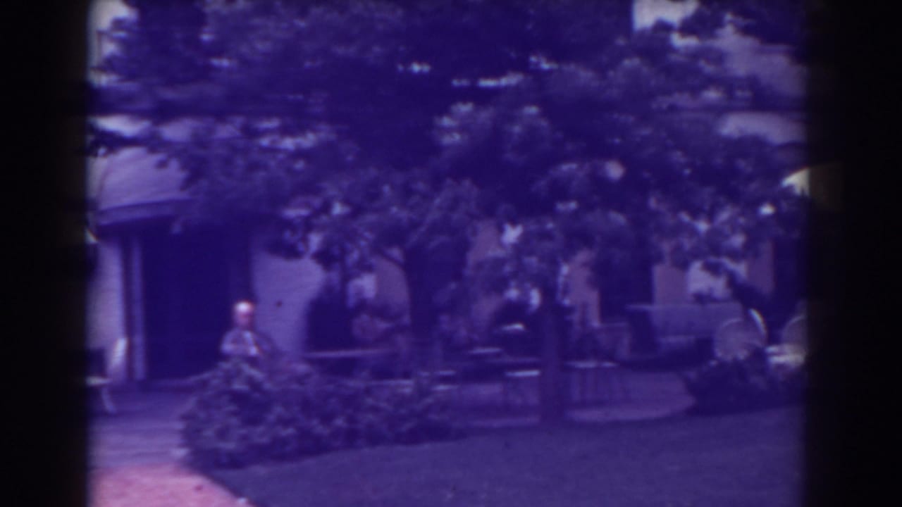 Courtyard exterior with arched awnings, patio furniture, shrubs, trees, and a man standing near the building.