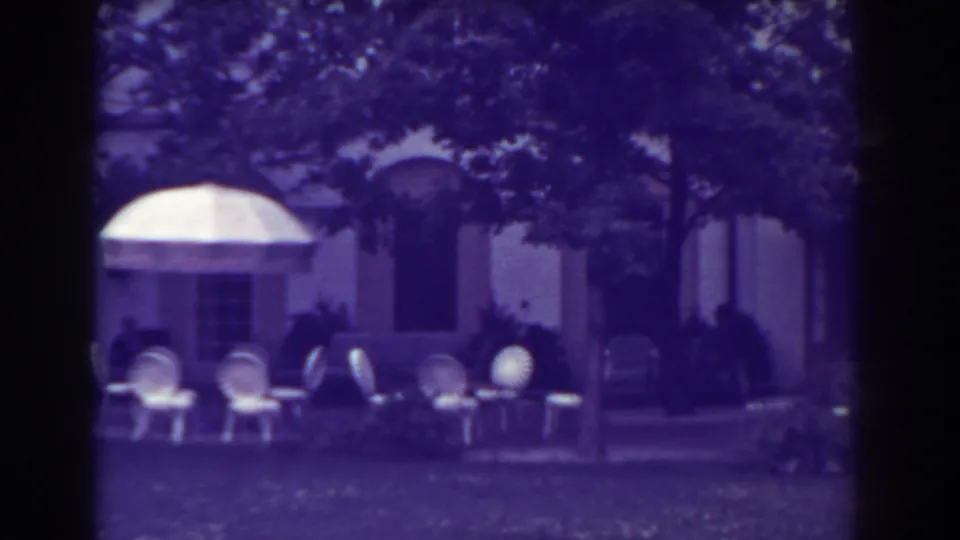 Atlantic City home-movie frame from 1938 with white patio seating, a light awning, trees, lawn, and a large shaded facade.