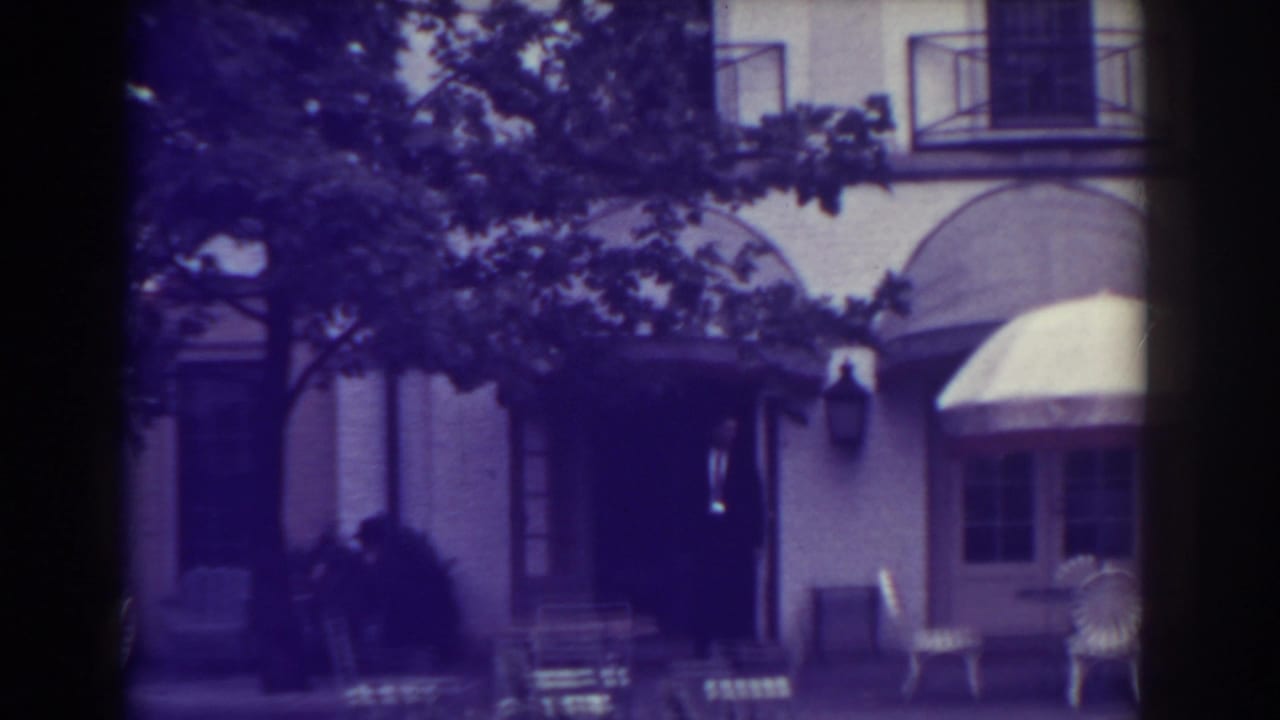 Building entrance with arched awnings, patio chairs, and shaded tree branches.