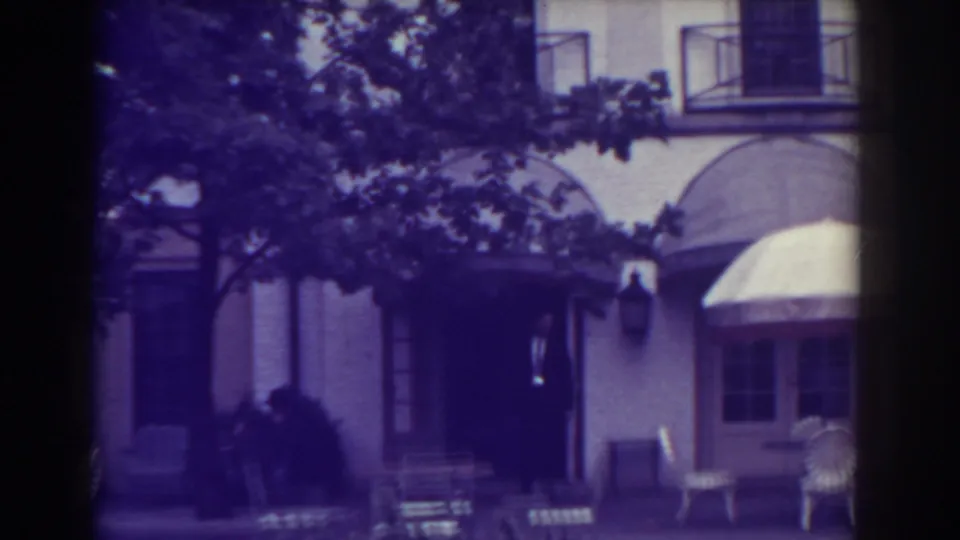 1938 Atlantic City frame with arched awnings over a building entrance, white patio chairs, and tree shade across the facade.