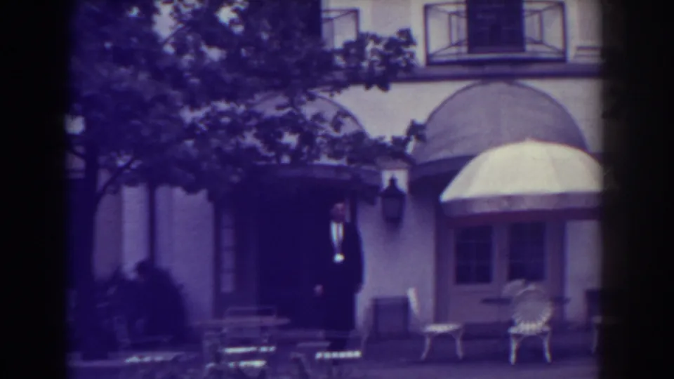1938 Atlantic City frame of a pale building exterior with doorway, awnings, patio chairs, and tree branches across the upper frame.
