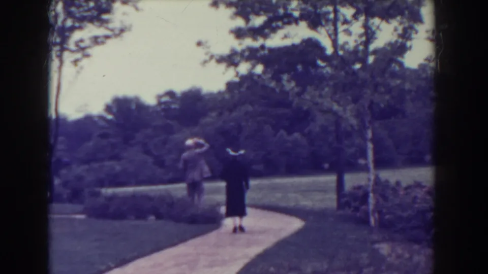 A man in a light suit and a woman in dark attire walk away together along a curved park path in 1938 Atlantic City footage.