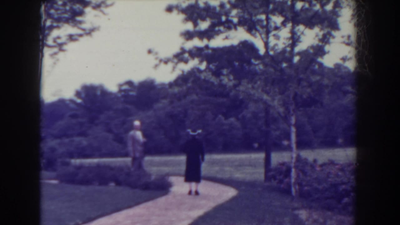 Two adults walk away on a curved garden path bordered by lawn and trees.