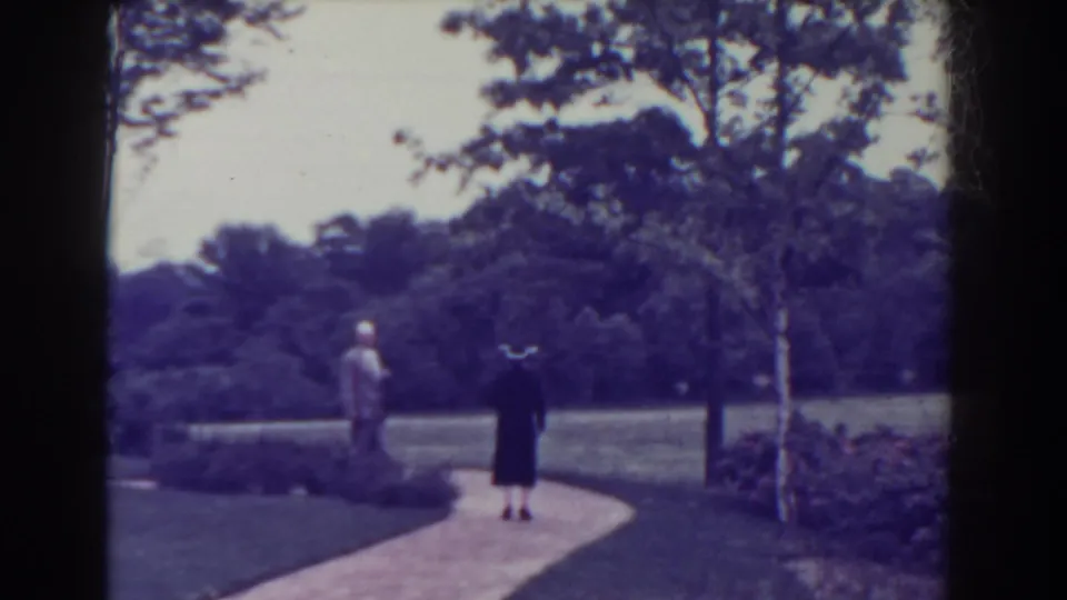 In 1938 Atlantic City home-movie footage, a man and woman walk away along a curved garden path in a leafy park setting.